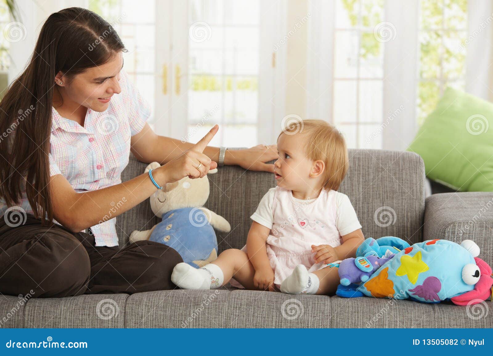 Babygirl de ensino da matriz. Sira de mãe ao babygirl de ensino que senta-se no sofá em casa, sorrindo.