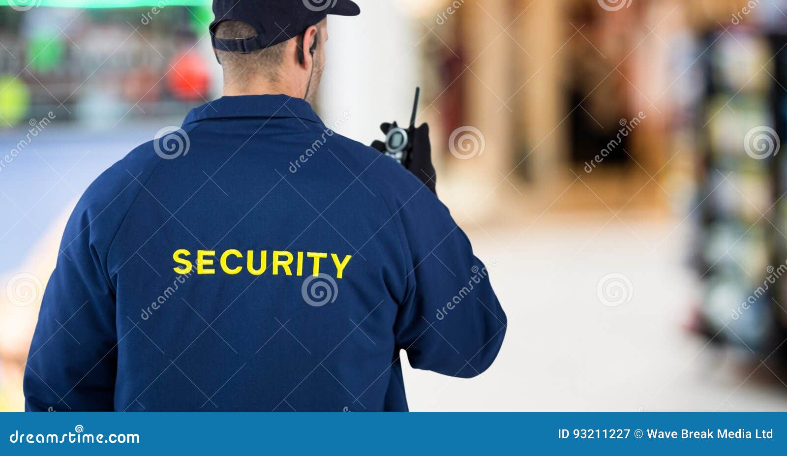 Back of Security Guard with Walkie Talkie Against Blurry Shopping