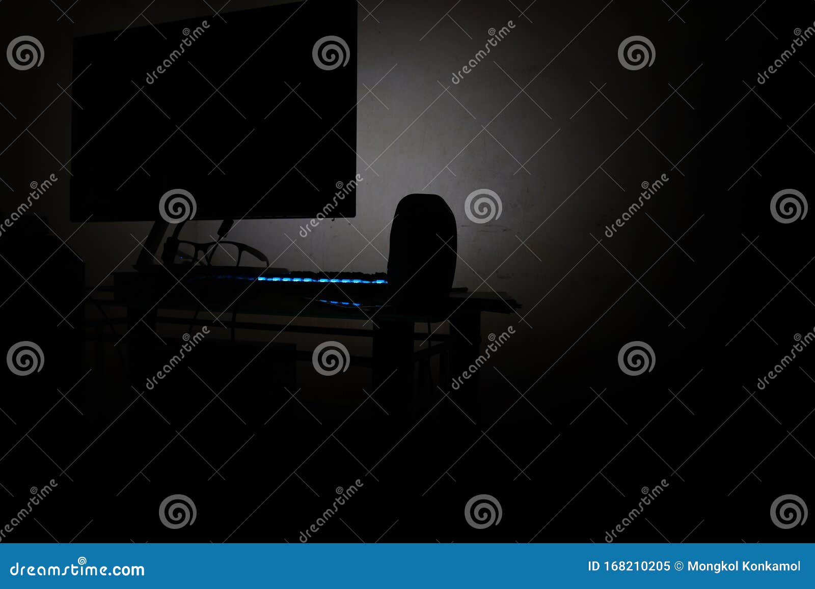 back view of computer in the dark room with blue led keybord and glasses and speaker, no people, not focused in picture