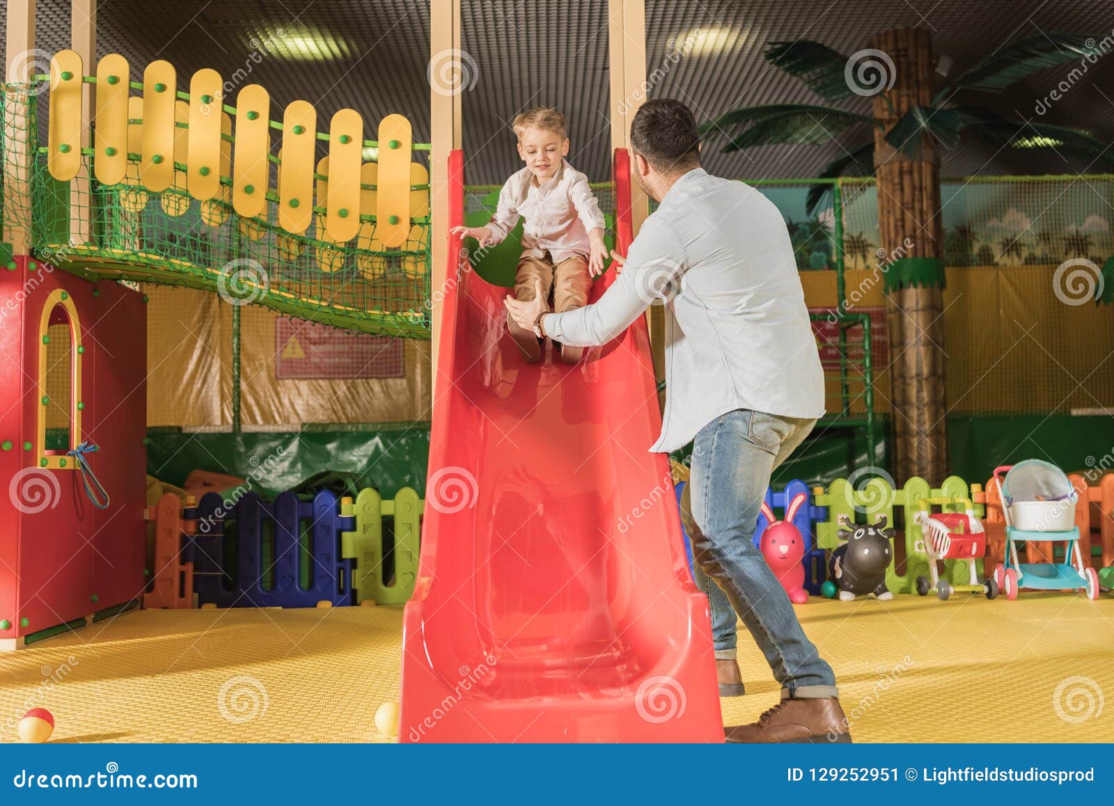back view of father looking at little son playing on slide