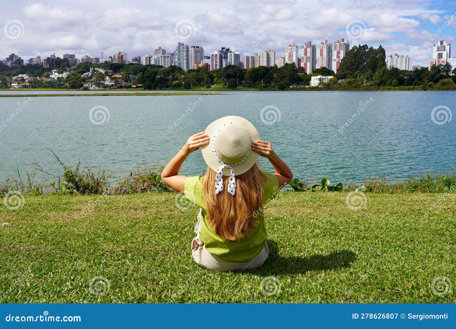 back view of girl with hat sitting on grass in barigui park, curitiba, brazil