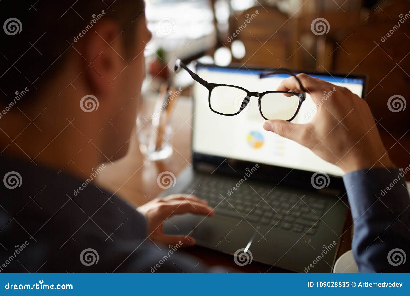 back view of man hand holding eyeglasses in front of laptop screen with charts and diagrams. poor eyesight threatment