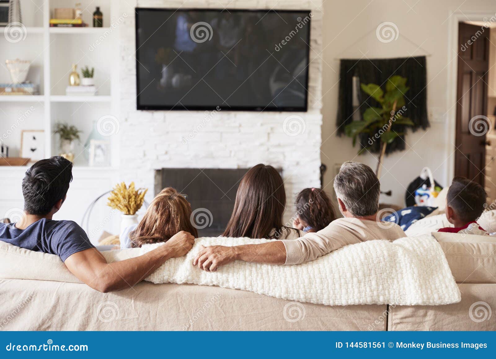 back view of three generation hispanic family sitting on the sofa watching tv