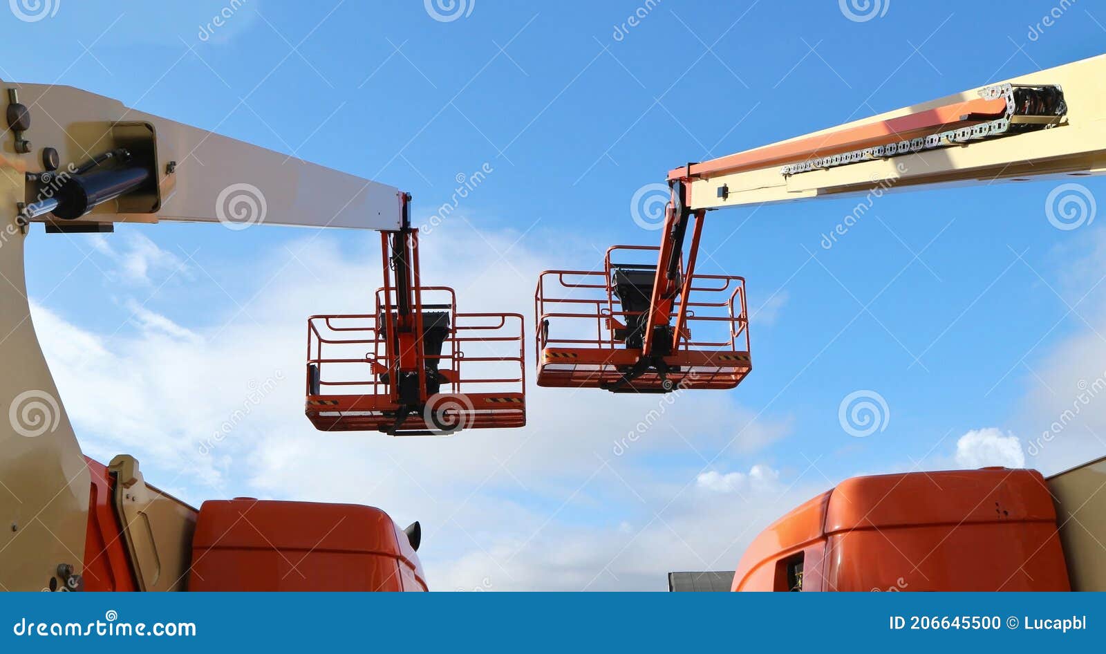 back view of two aerial work platforms against blue sky with clouds.
