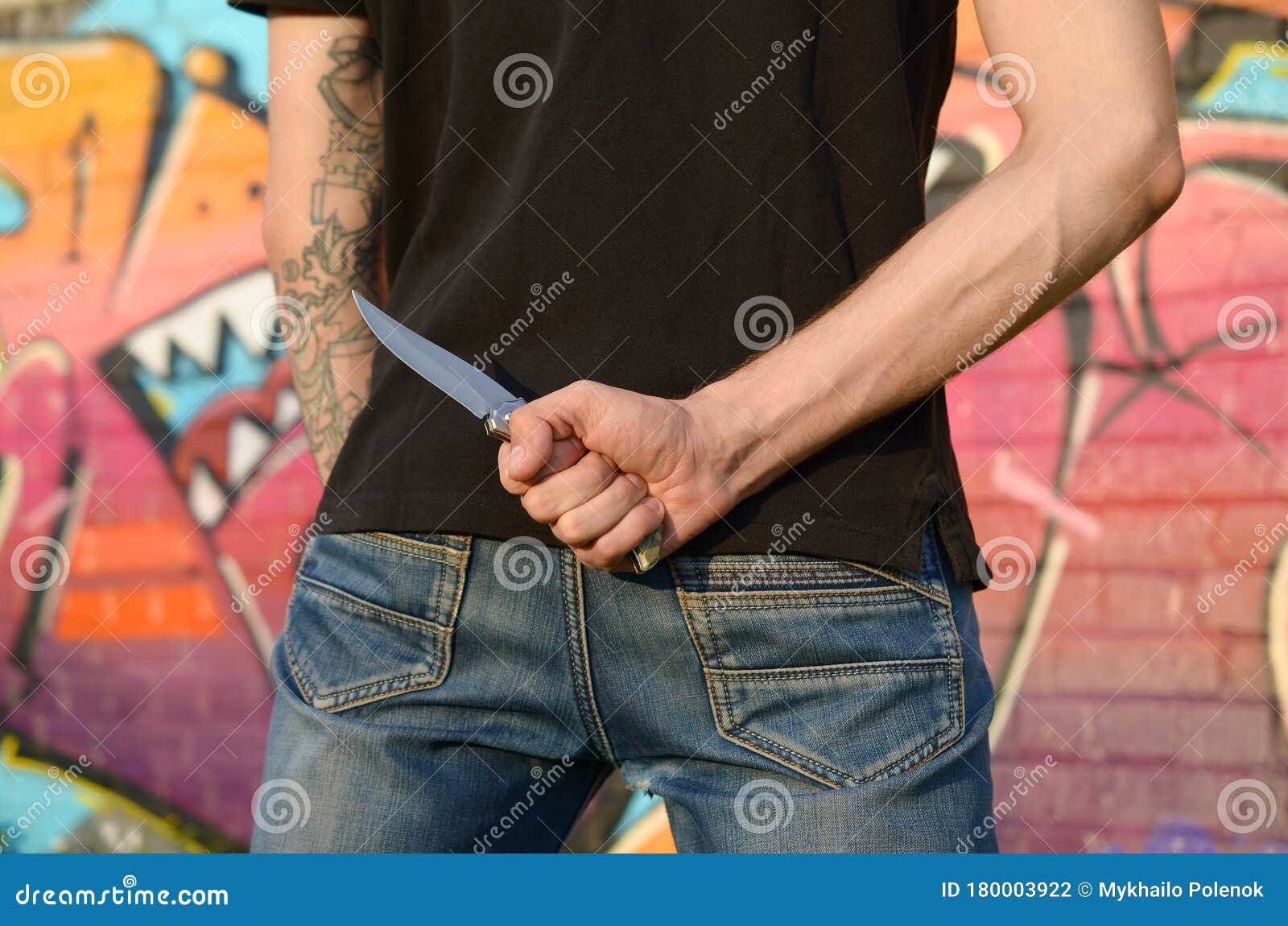 back view of young caucasian man with knife in his hand against ghetto brick wall with graffiti paintings. concept of criminal