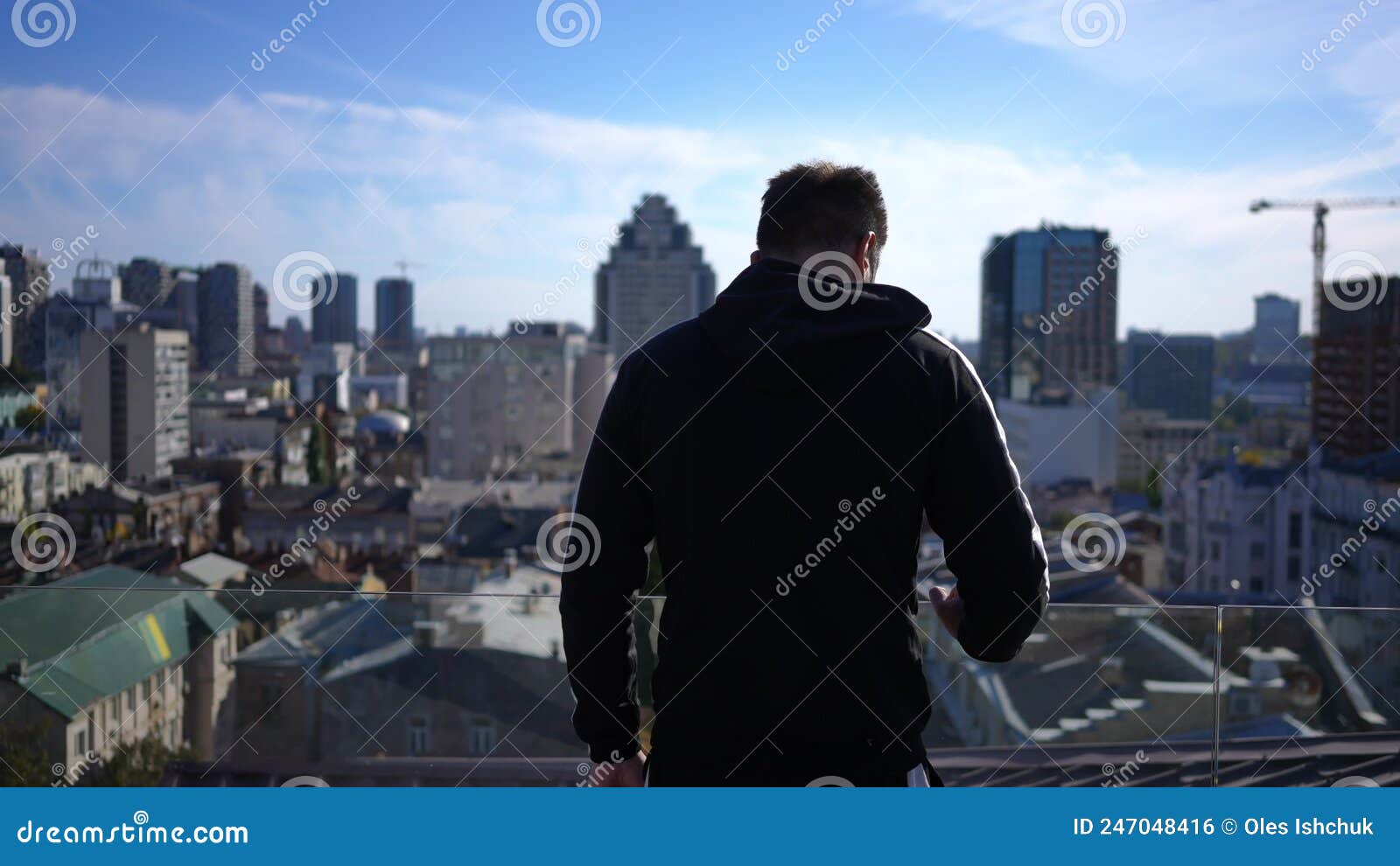 Back View Young Man Walking To Glass Fence on Rooftop Looking at
