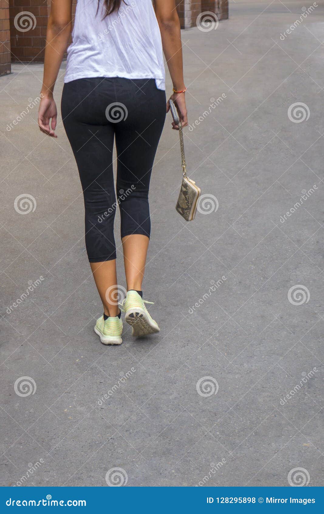 back of a woman walking holding a hanging pocketbook in yoga pan