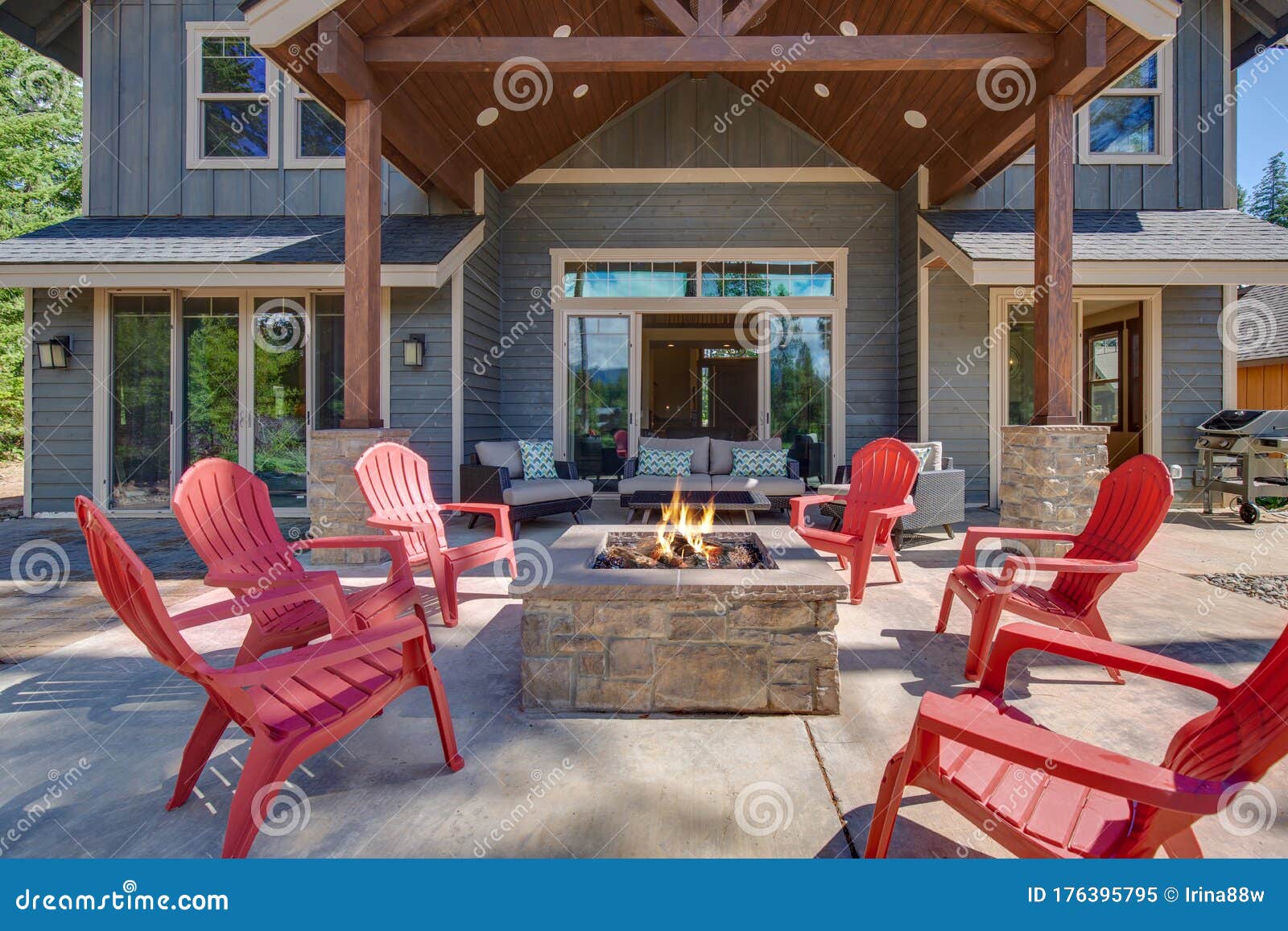 back yard with fire pit and red chairs near newly bild luxury real estate home with forest biew and green grass