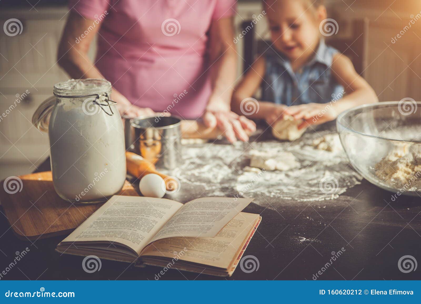 background image cookbook, table, rolling pin, focus on the foreground. girl and her grandmother cooking on kitchen.