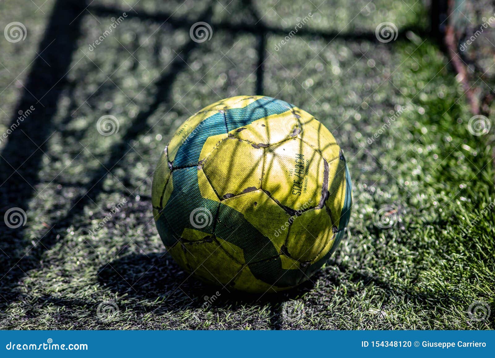 Background. yellow and green soccer ball on a synthetic five-a-side football field with the shadow of the goal net..