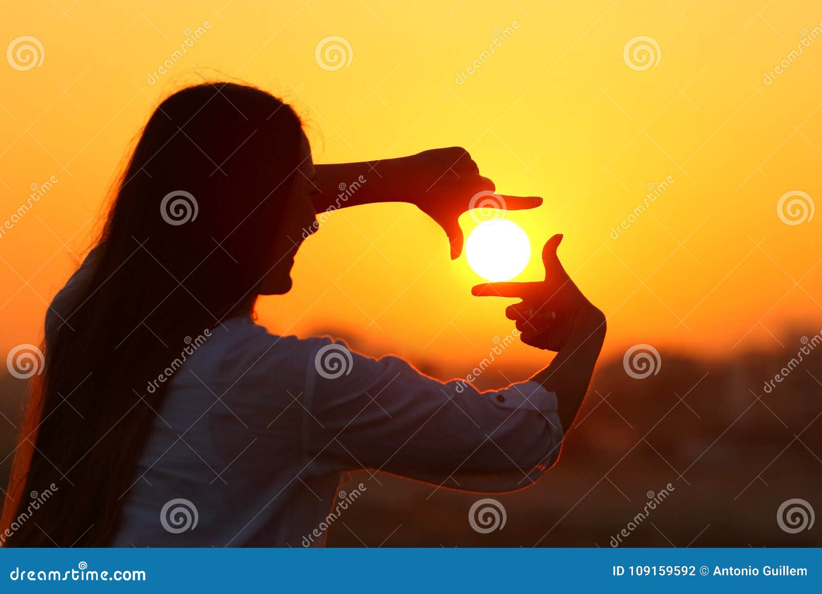 woman framing sun with fingers at sunset