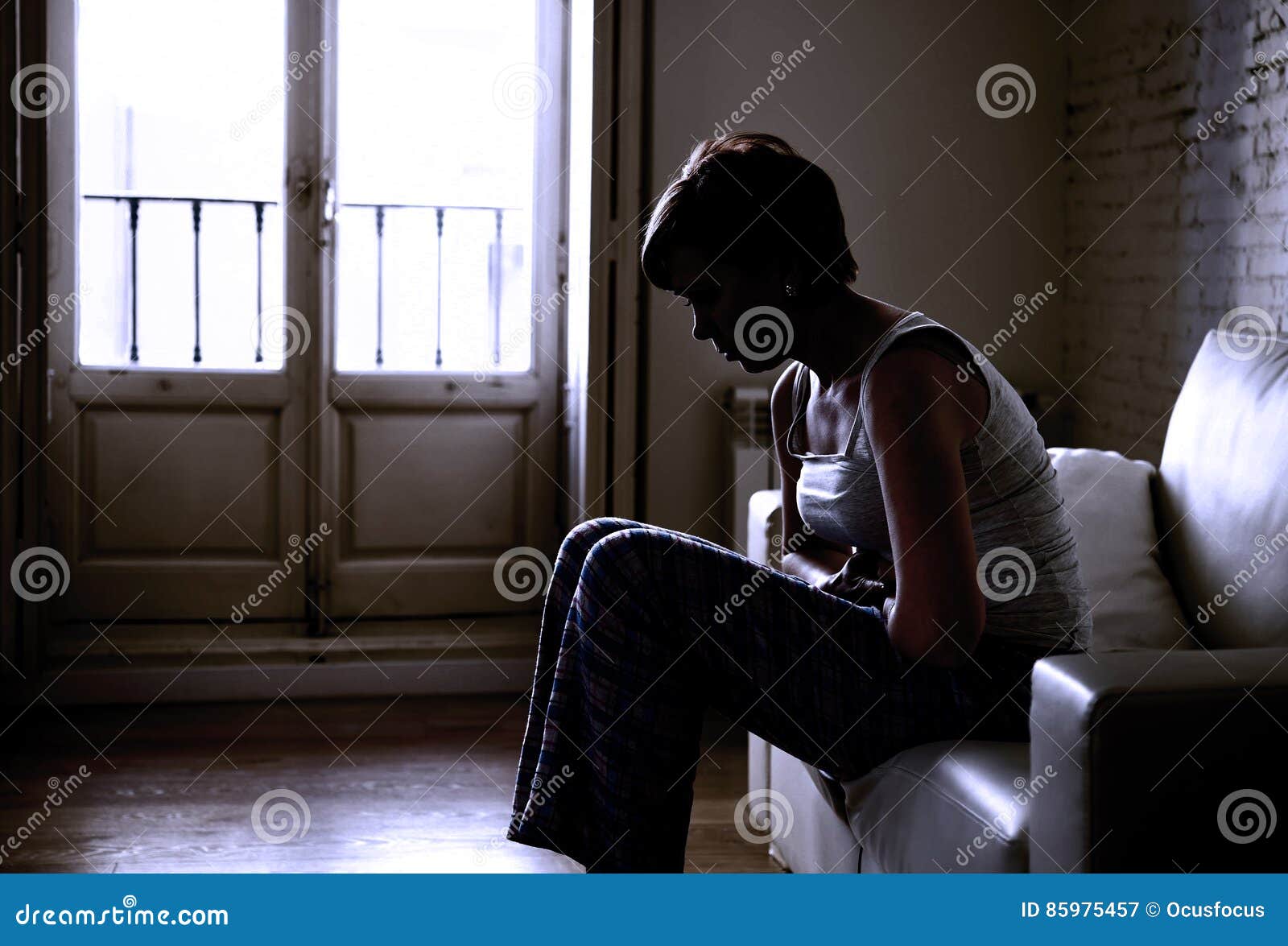 backlit silhouette of young woman holding hurting tummy suffering stomach cramp and period pain