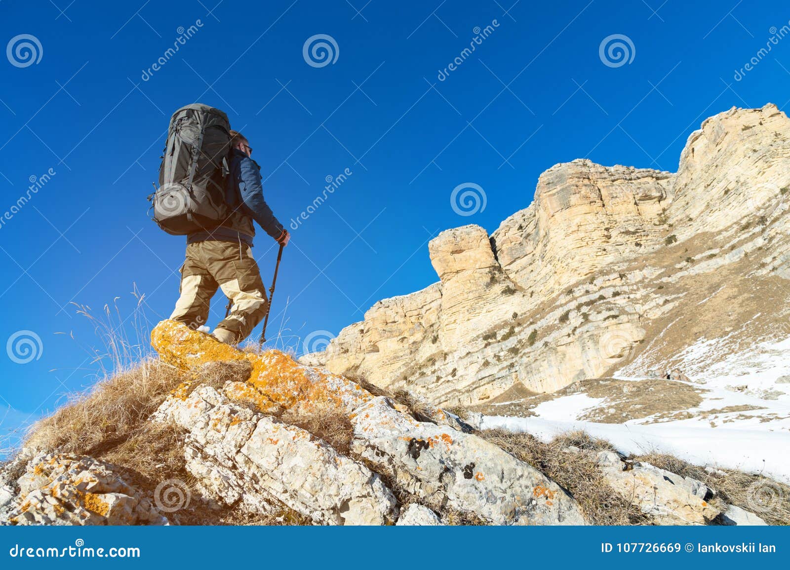 Backpacker with a Large Backpack and Sticks Ascends To the Rock Against