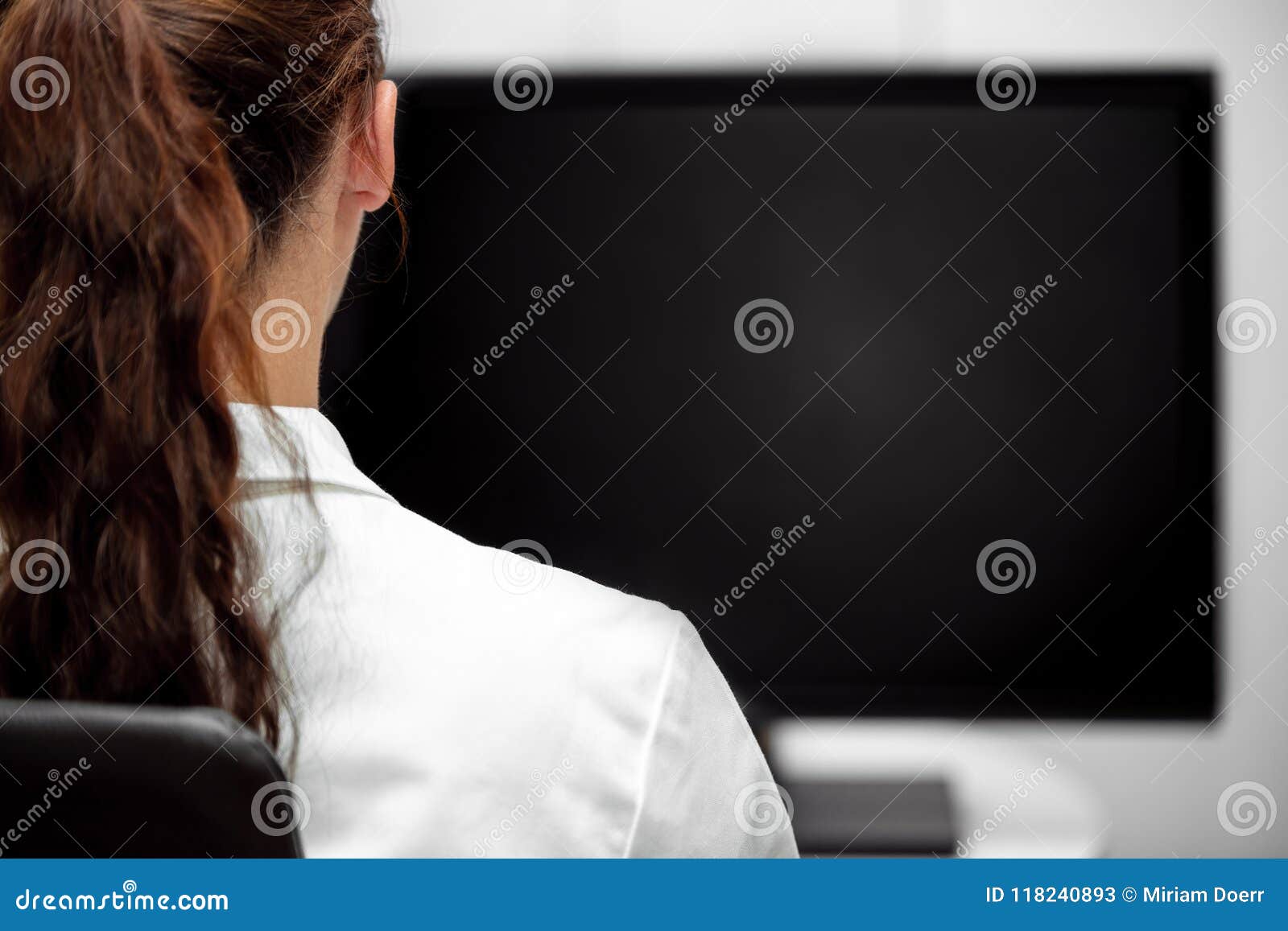 backview, young lab assistent or female doctor looking at a black desk or monitor