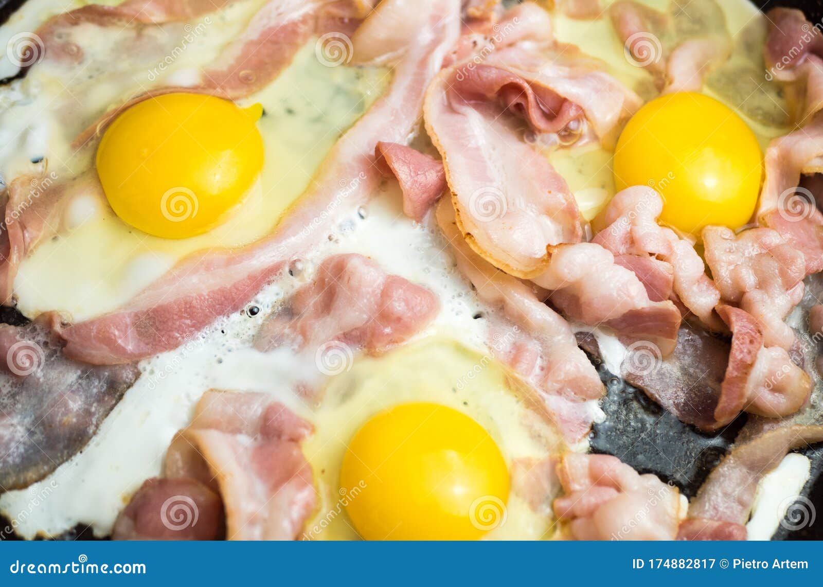 Bacon is Fried in a Black Pan. Fat in Boiling Fat. Scrambled Eggs