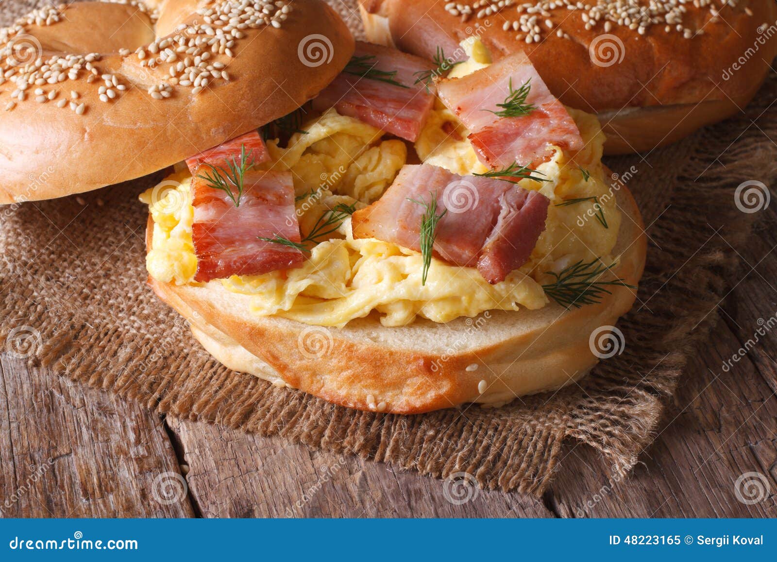 Bagel com ovos mexidos e close-up do bacon horizontal. Bagel com ovos mexidos e close-up do bacon na tabela horizontal