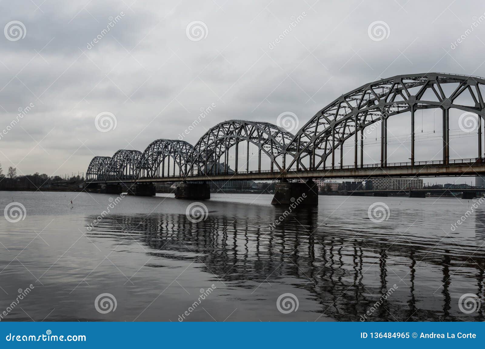 Bahnbrücke über Daugava-Fluss Lettland. Zug überschreitet über ein Eisen und eine ikonenhafte Brücke über Daugava-Fluss während eines kalten Wintertages Wolken sind vom Regen schwer und sind schwarz Wir sind in Riga, Lettland