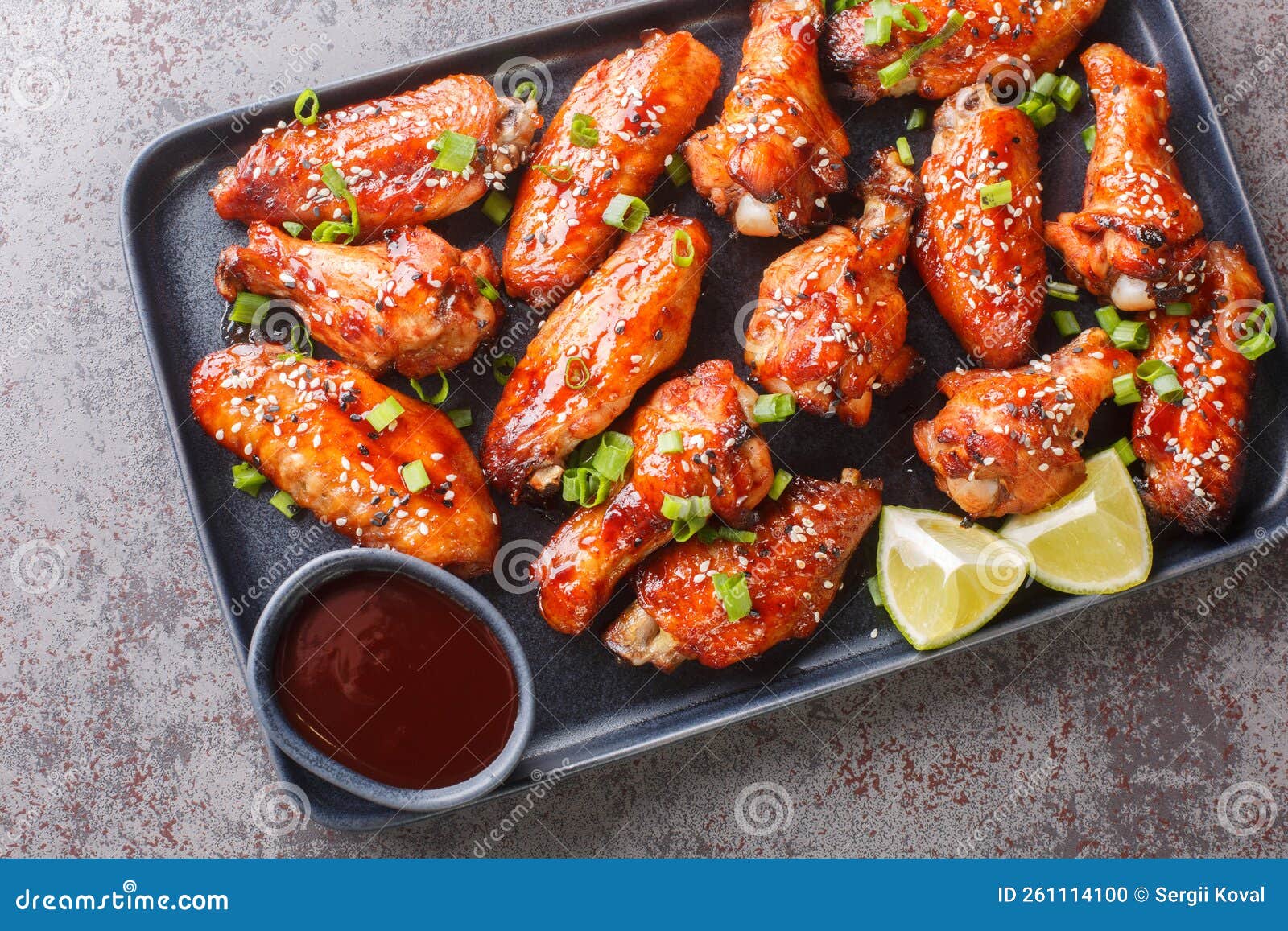 baked hoisin sauce chicken wings with sesame served with green onion, lime close-up in a plate . horizontal top view