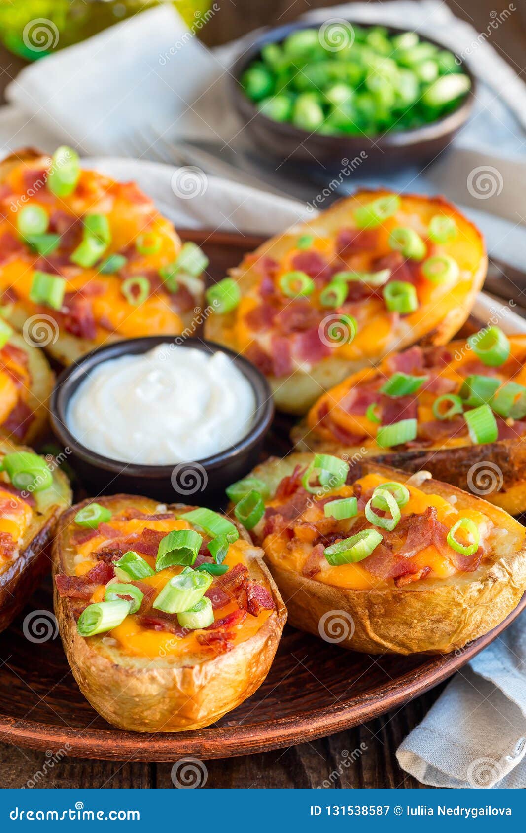 baked loaded potato skins with cheddar cheese and bacon garnished with scallions and sour cream, vertical