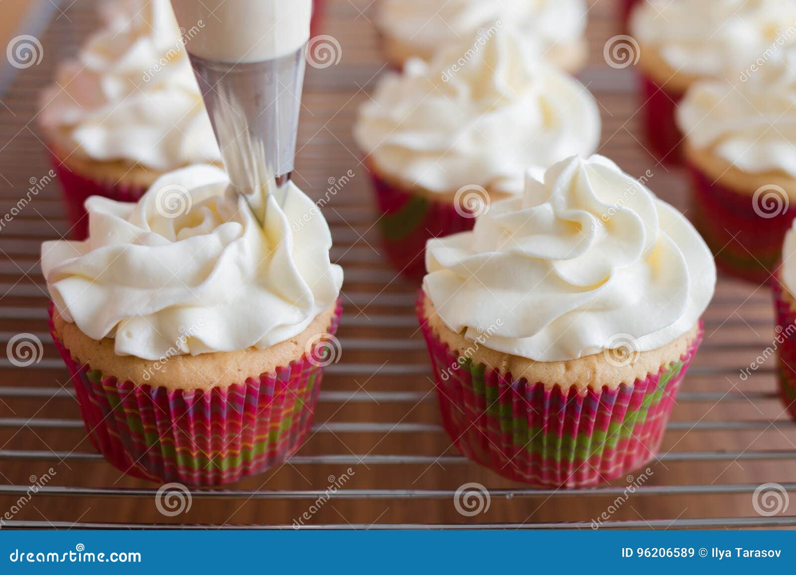 baker decorates muffins with cream and confectionery nozzles