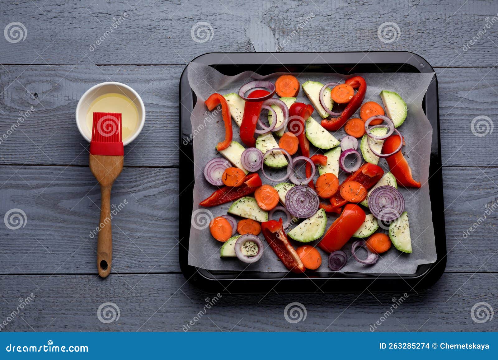 Baking Pan with Parchment Paper and Raw Vegetables on Grey Wooden Table