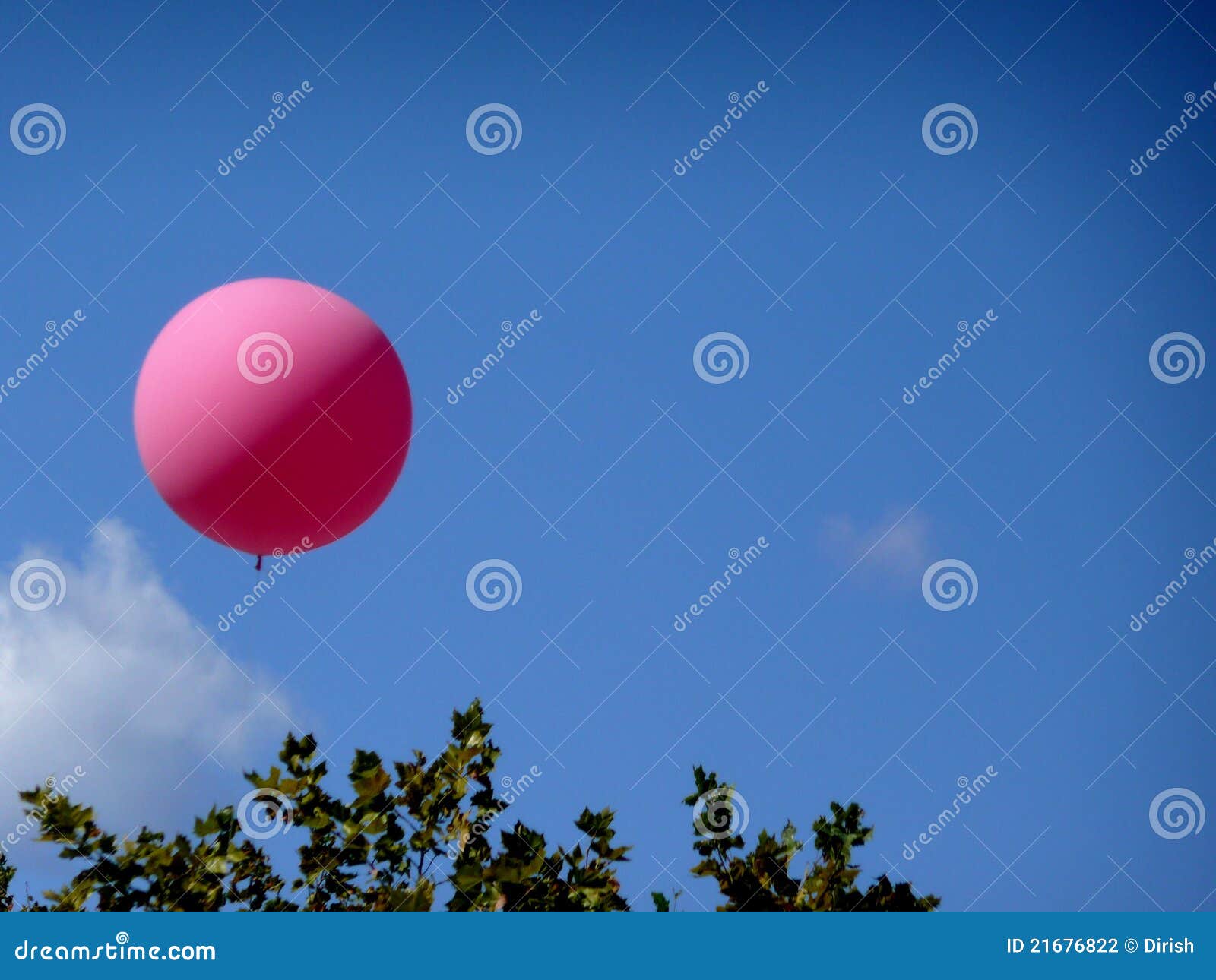 Un ballon rose flotte au-dessus des arbres dans le ciel bleu