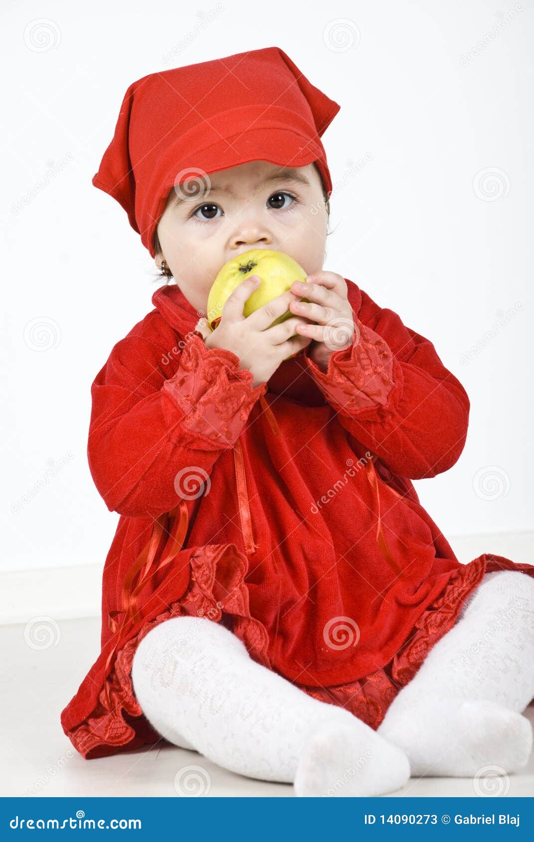 Bambino che mangia mela. La ragazza del bambino che si siede sul pavimento si è vestita in vestiti rossi e nel cibo della mela verde. Controlli egualmente i <a href="http://www.dreamstime.com/children--rcollection13056-resi828293">bambini</a>