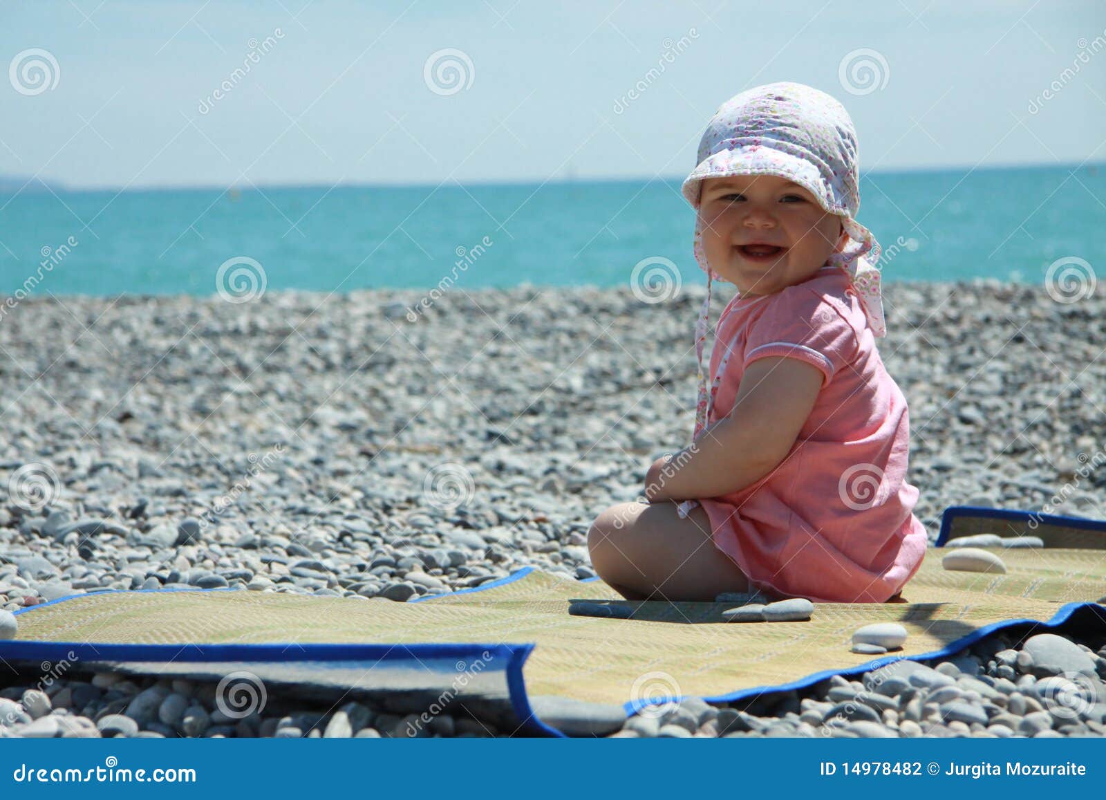 Bambino sulla spiaggia. Neonata (1 anno) che si siede sulla spiaggia rocciosa di Riviera francese e di sorridere