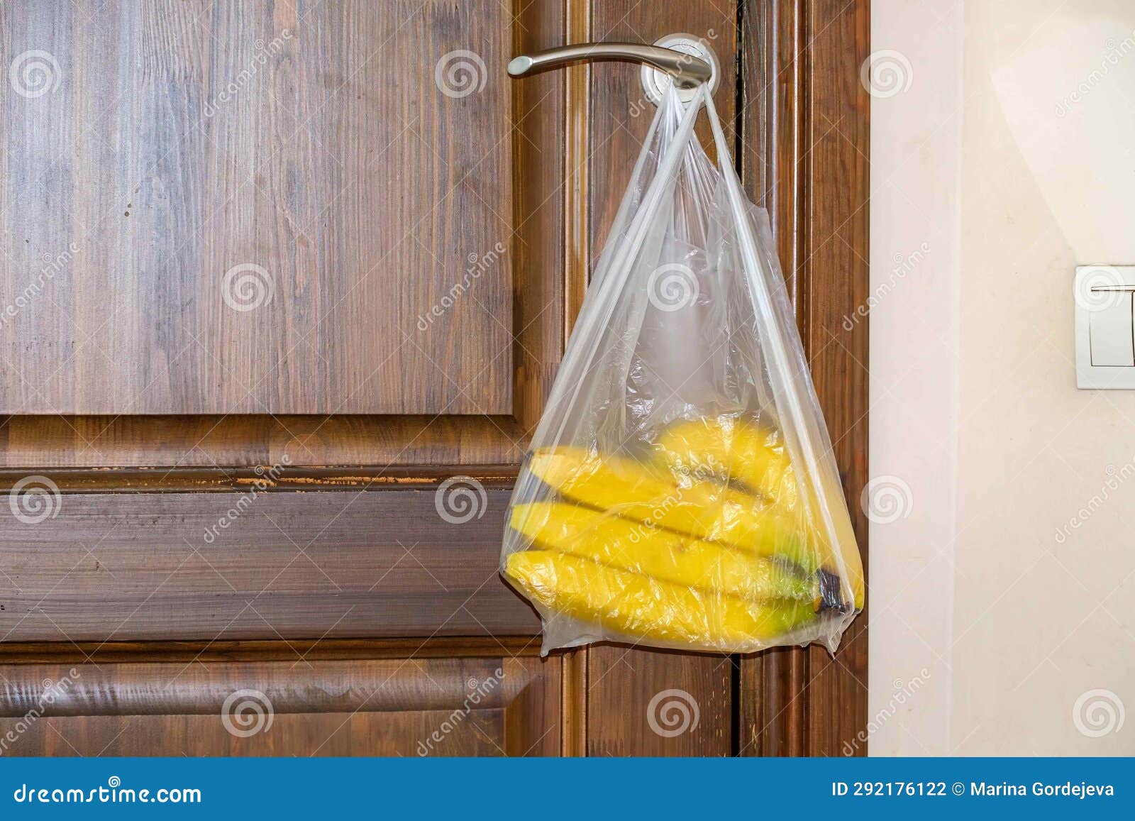 A Banana in a Plastic Bag Hangs on the Door Handle of a Wooden Door