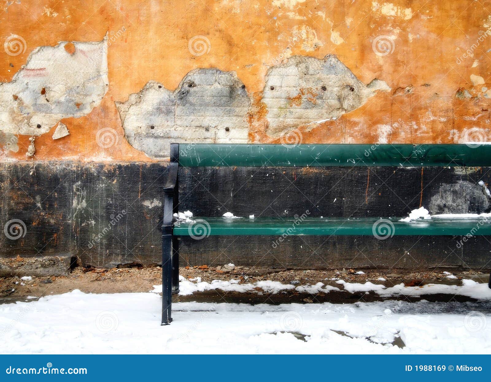 Banco y pared. Banco verde en nieve contra la pared de decaimiento del estuco