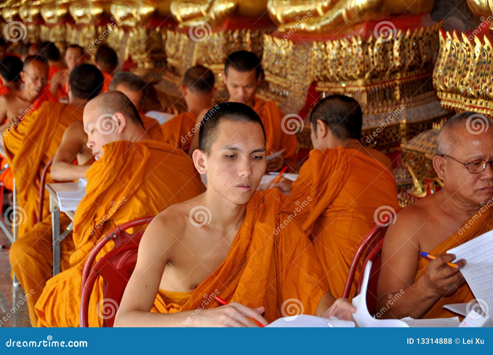 Bangkok, Thailand: Monniken bij Tempel Suthat. Monniken die traditionele oranje robes dragen die terwijl gezet bij lijsten onder een rij van vergulde Buddhas bij de tempel van Wat Suthat in Bangkok, Thailand - Lee Snider Photo werken.