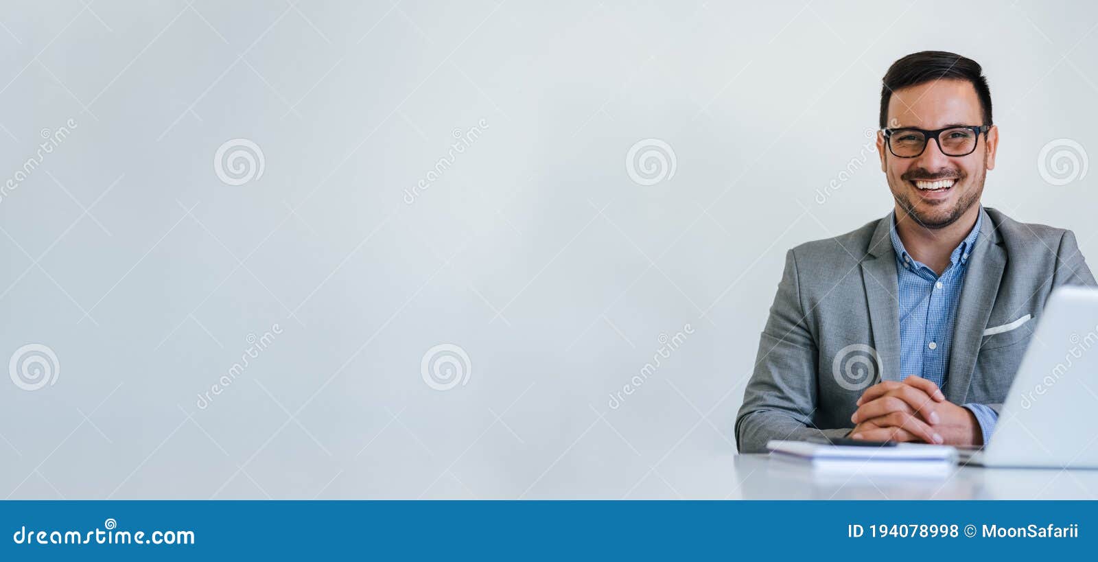 banner panorama portrait of young smiling cheerful businessman manager entrepreneur with eyeglasses sitting at desk in office or