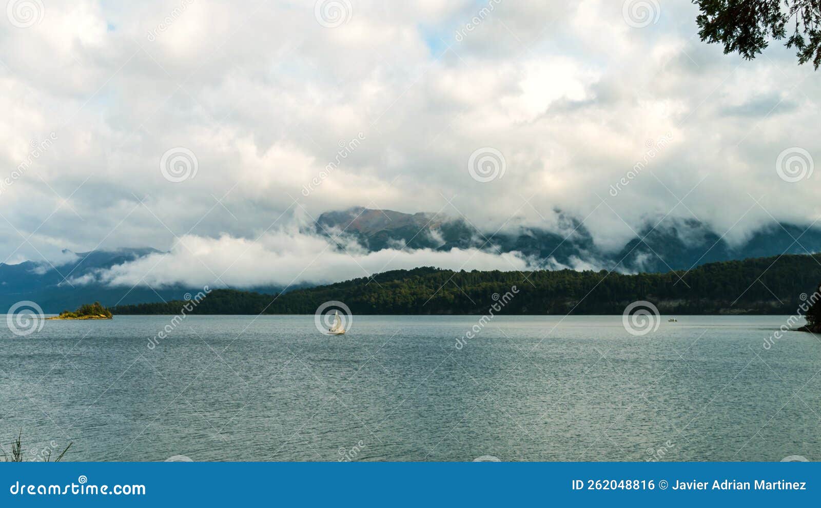 sailboat navigating a calm lake with low clouds and mountains in the background. villa la angostura, argentina