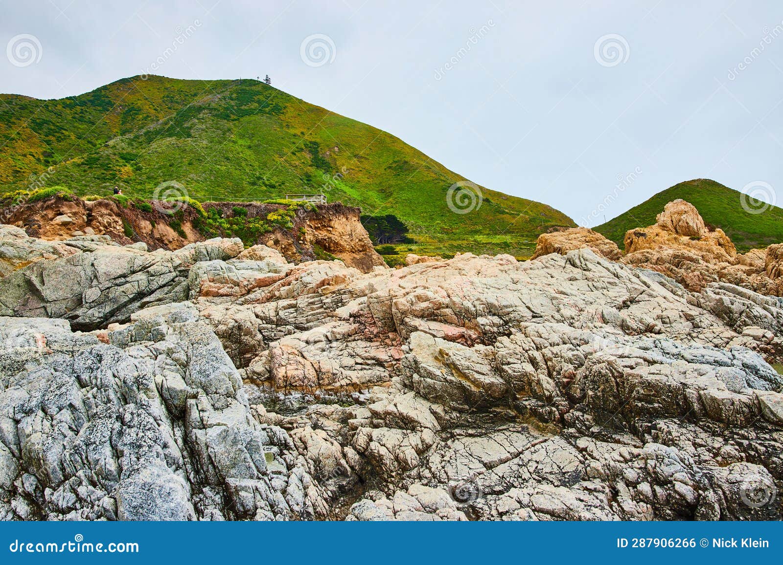 baren rock cliff face in jagged crags with distant green mountainous hillside and overcast sky