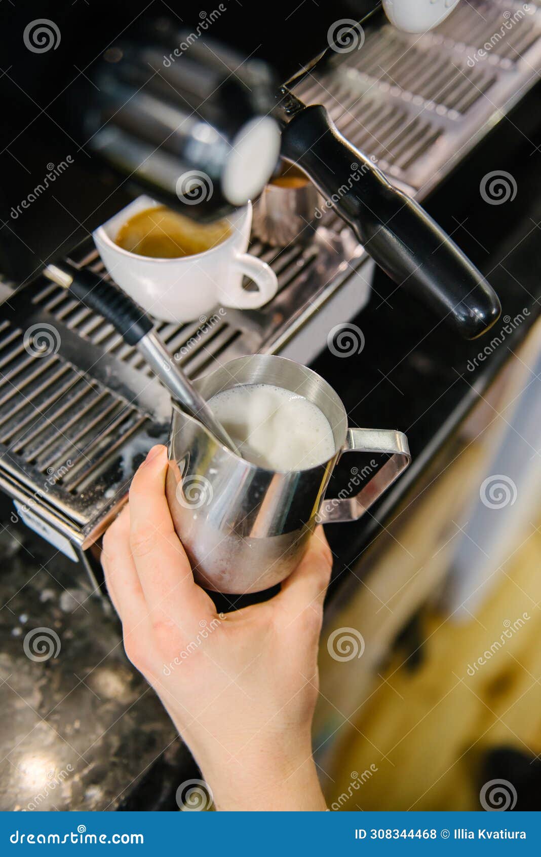 barista froths milk for coffee. there is a cup of freshly brewed coffee in the coffee machine