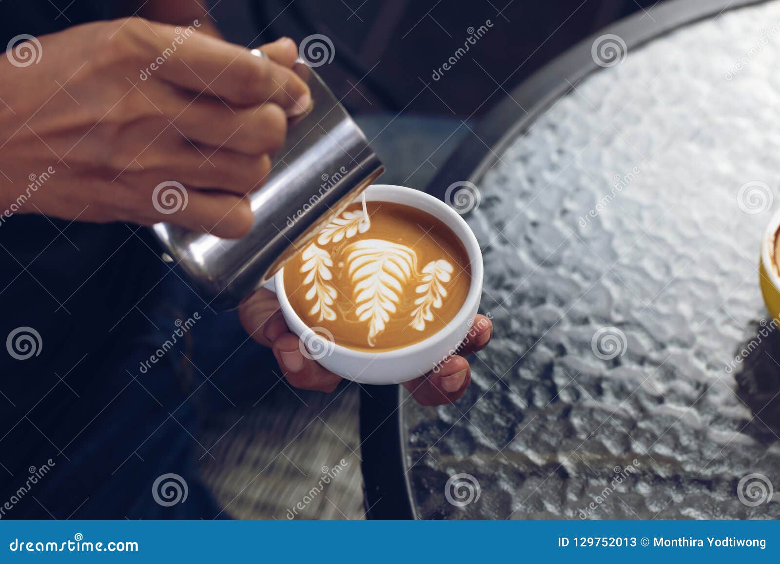 barista pouring milk foam for making coffee latte art with pattern the leaves in a cup