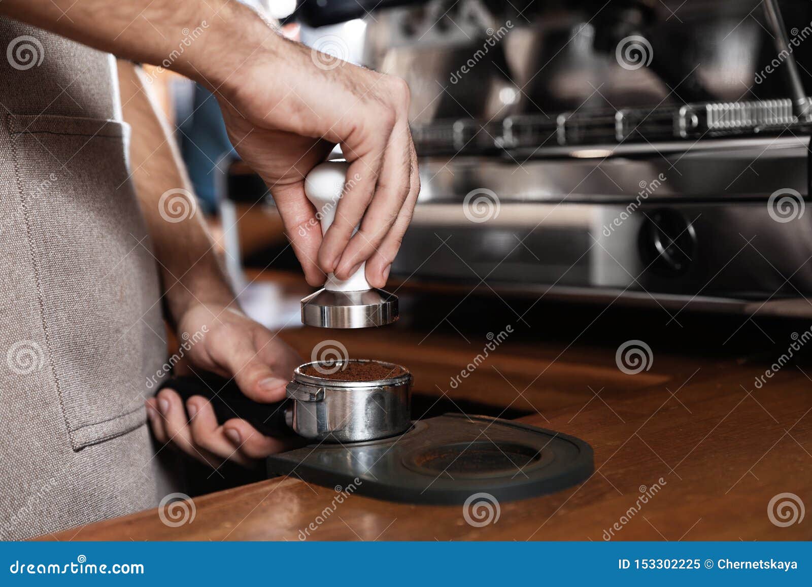 barista tamping milled coffee in portafilter at bar counter, closeup