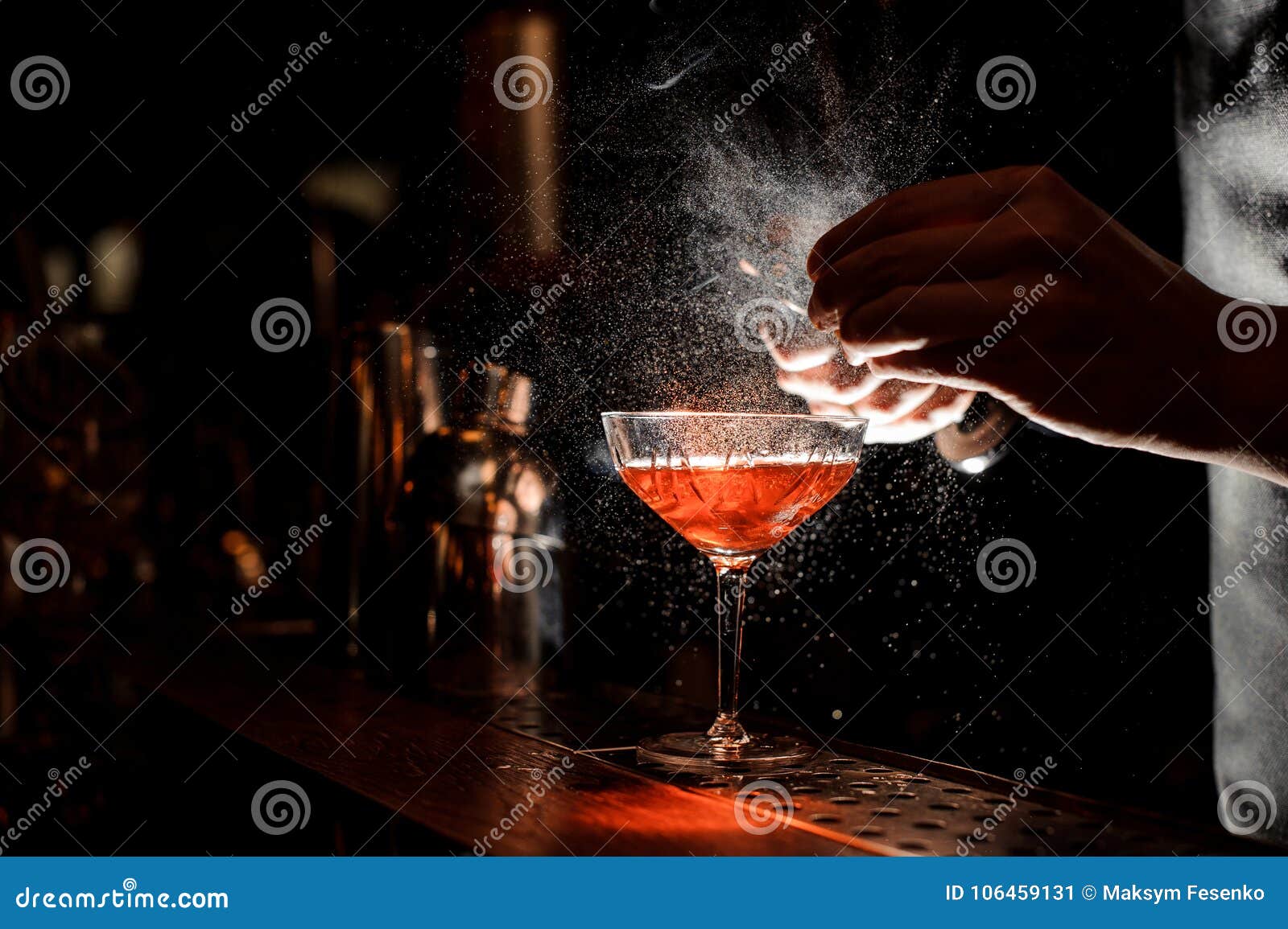 barmans hands sprinkling the juice into the cocktail glass