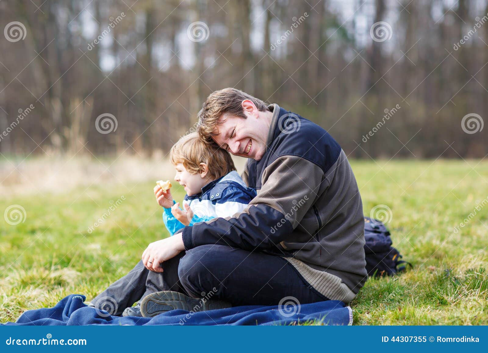 Barnet avlar och den lilla sonen som har picknicken och rolig near skogla. Det lyckliga barnet avlar och den lilla sonen som har picknicken och den roliga near skogsjön, naturen på den kalla våren eller höstdagen