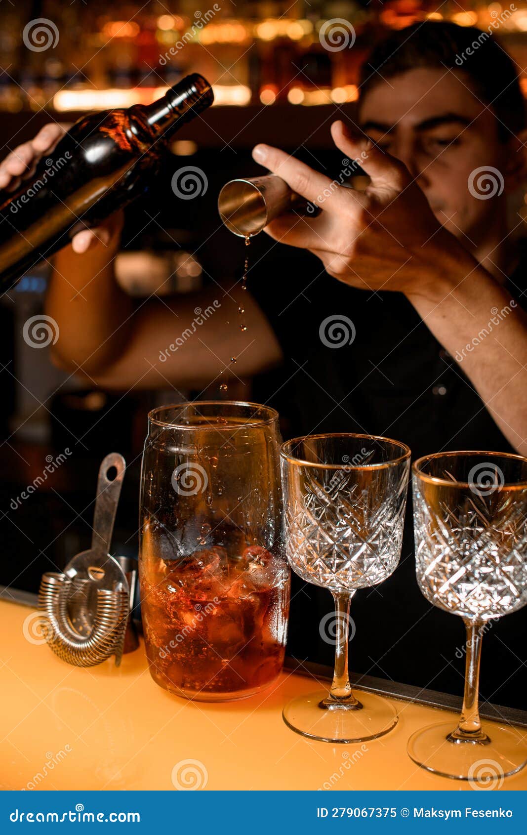 Bartender Holds In Hand Steel Jigger And Pours Drink From Bottle