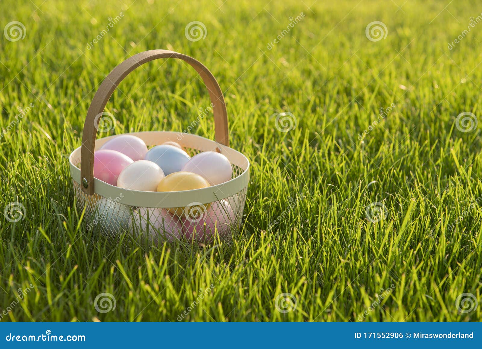 Basket with Pastel Colored Easter Eggs on a Grass Field Stock Photo
