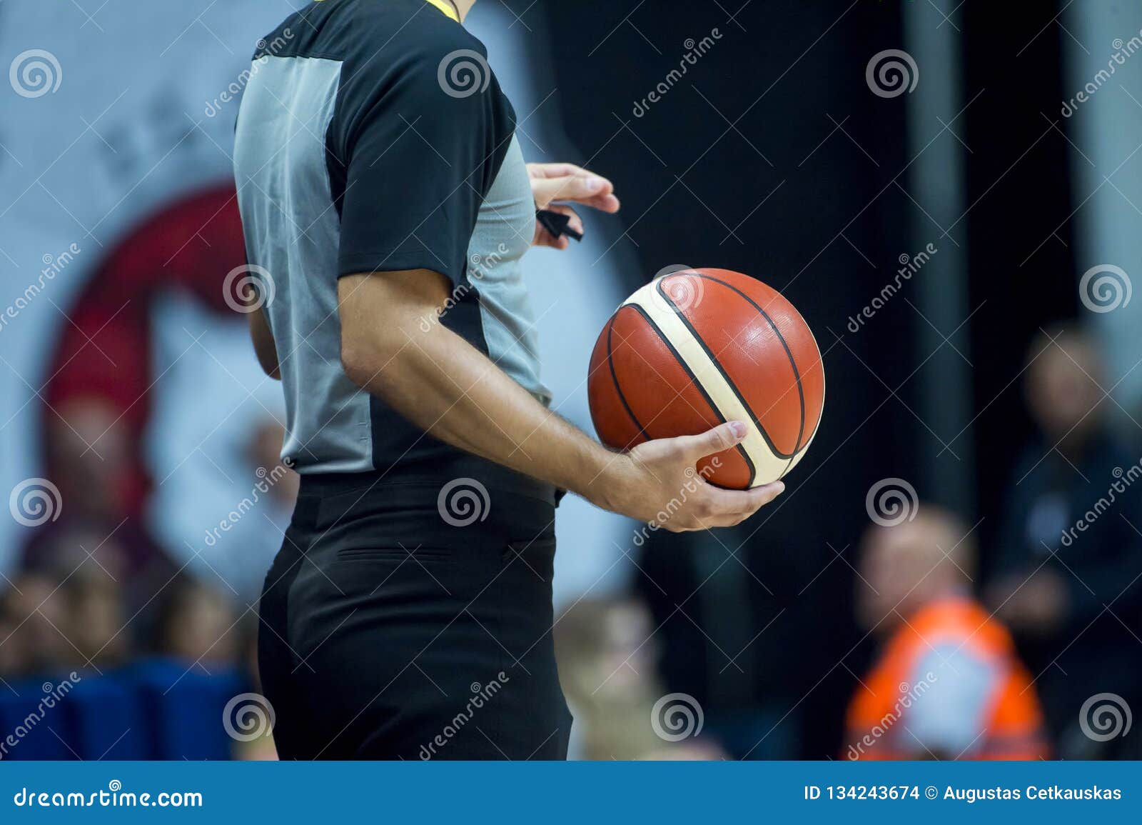 Basketball Referee Holding a Basketball at a Game in a Crowded Sports