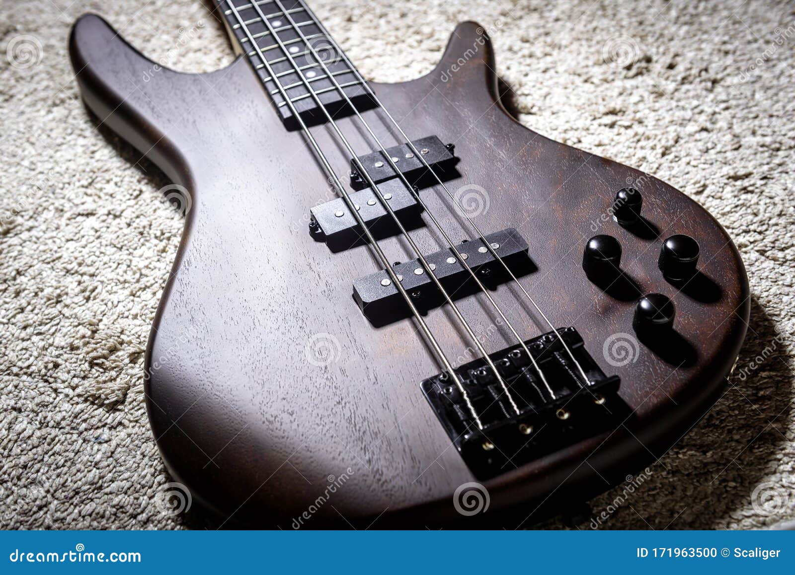 bass electric guitar with four strings. popular rock musical instrument. close view of brown bass on carpet