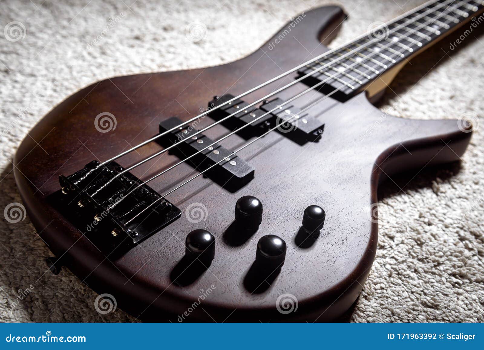 bass guitar with four strings. popular rock musical instrument. close view of brown electric bass on carpet