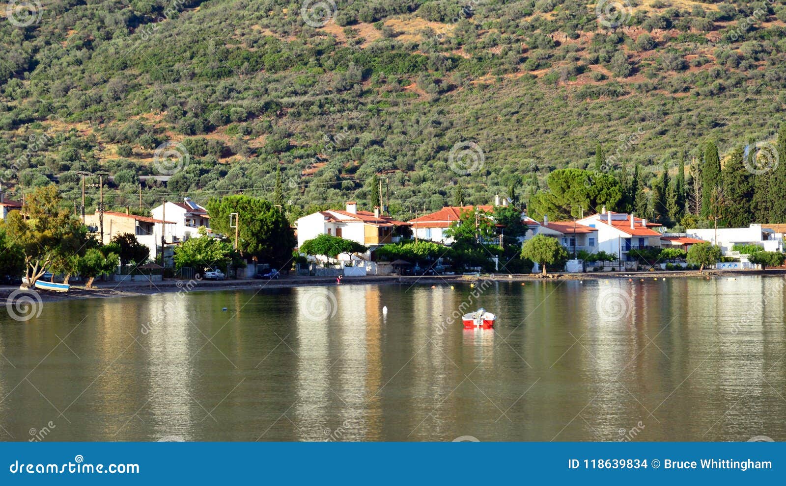 Baía do Golfo de Corinto, fim da tarde, Grécia. A vista através de uma baía do Golfo de Corinto, Ormos Lemonias, às construções da vila da pesca e do feriado e oliveira cobriu montanhas, Panormos Fokidos, Grécia As reflexões verdes da montanha das montanhas no fim da tarde aquecem a luz