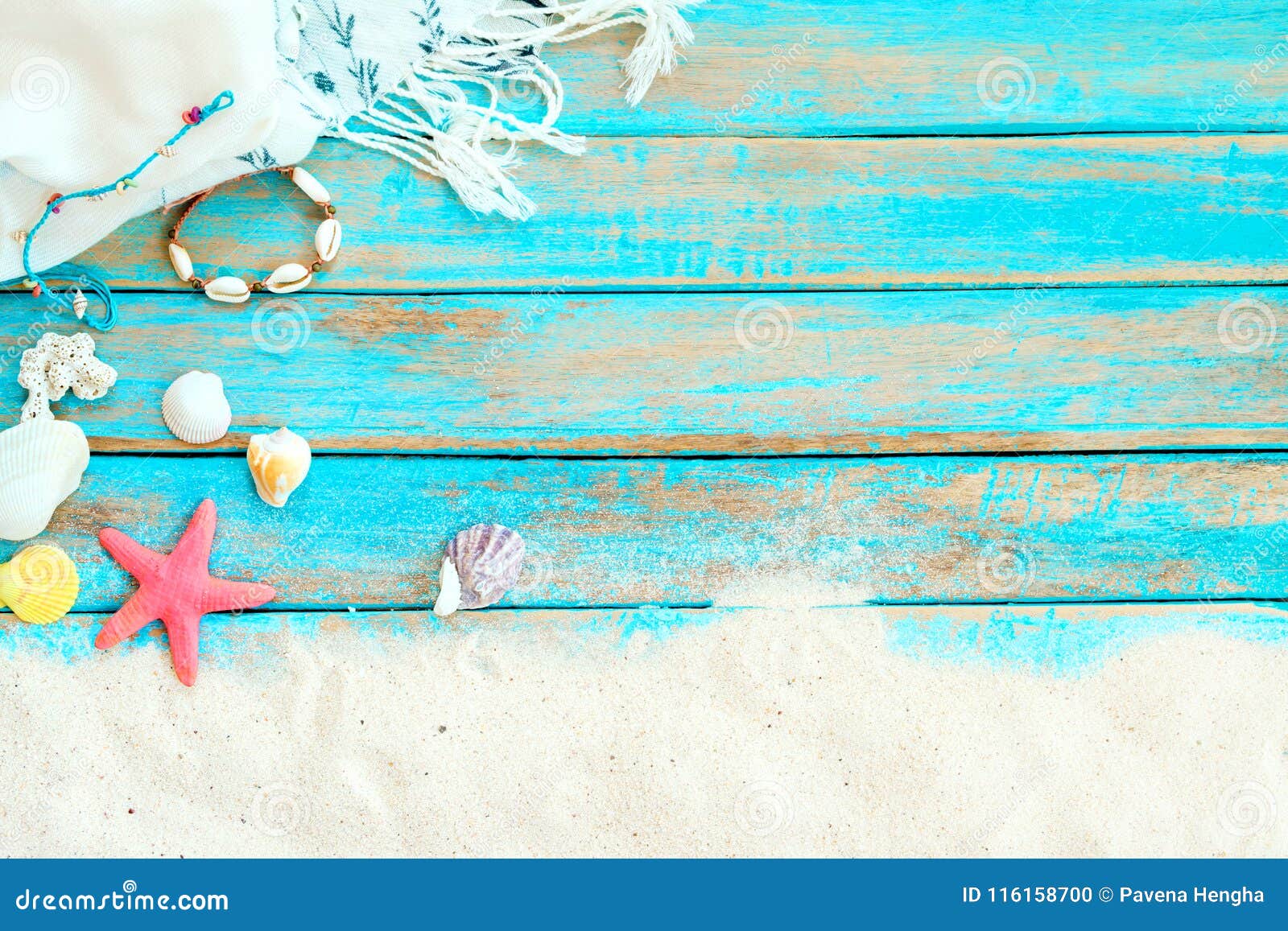top viwe of beach sand with white shawl, bracelet made of seashells, starfish, shells and coral on blue wooden background.