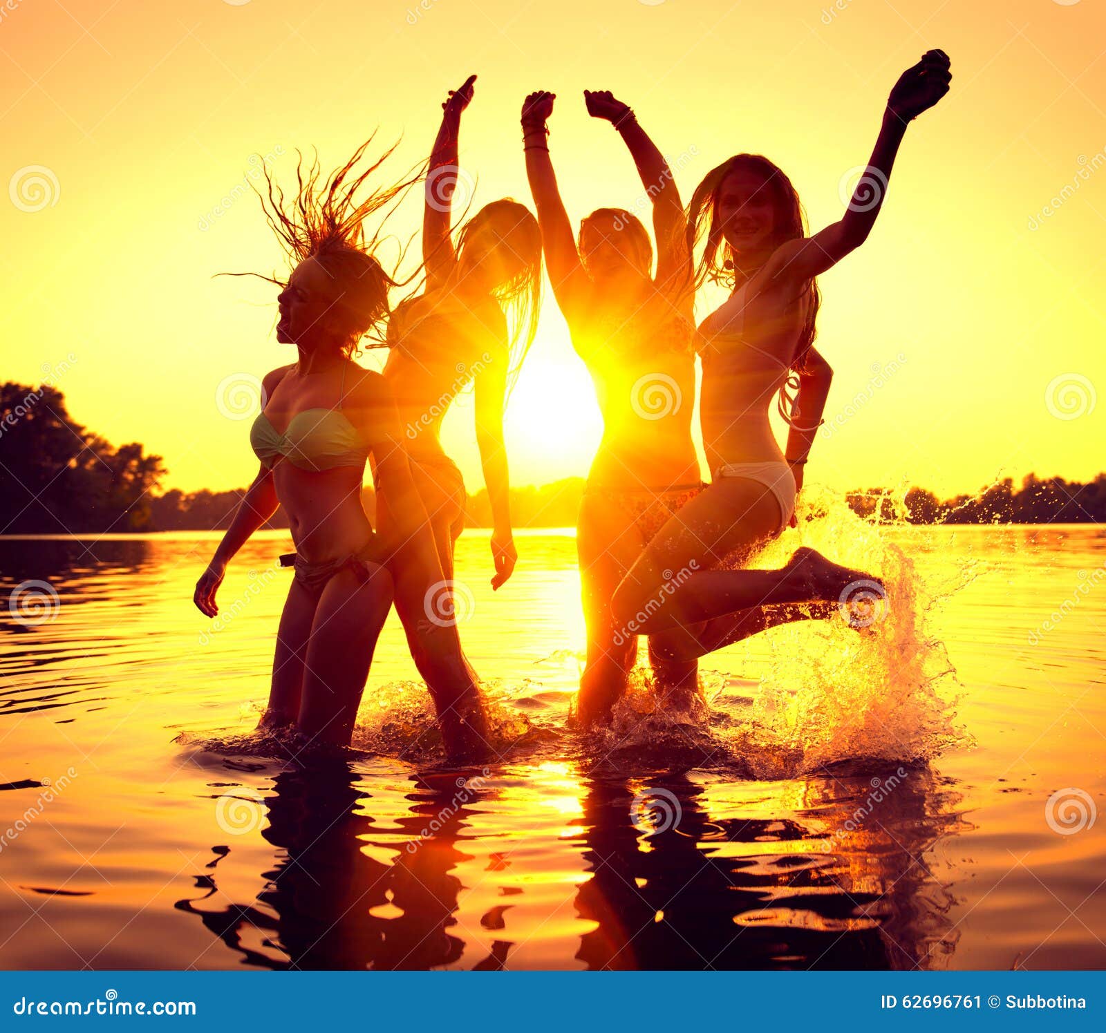 beach party. happy girls in water over sunset