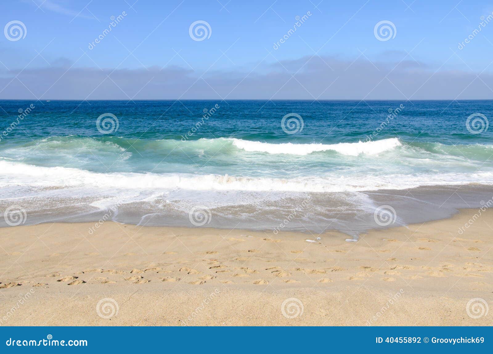 This is a picture of a beautiful beach in California, USA. The waves are crashing against the shore. There are footprints in the sand.