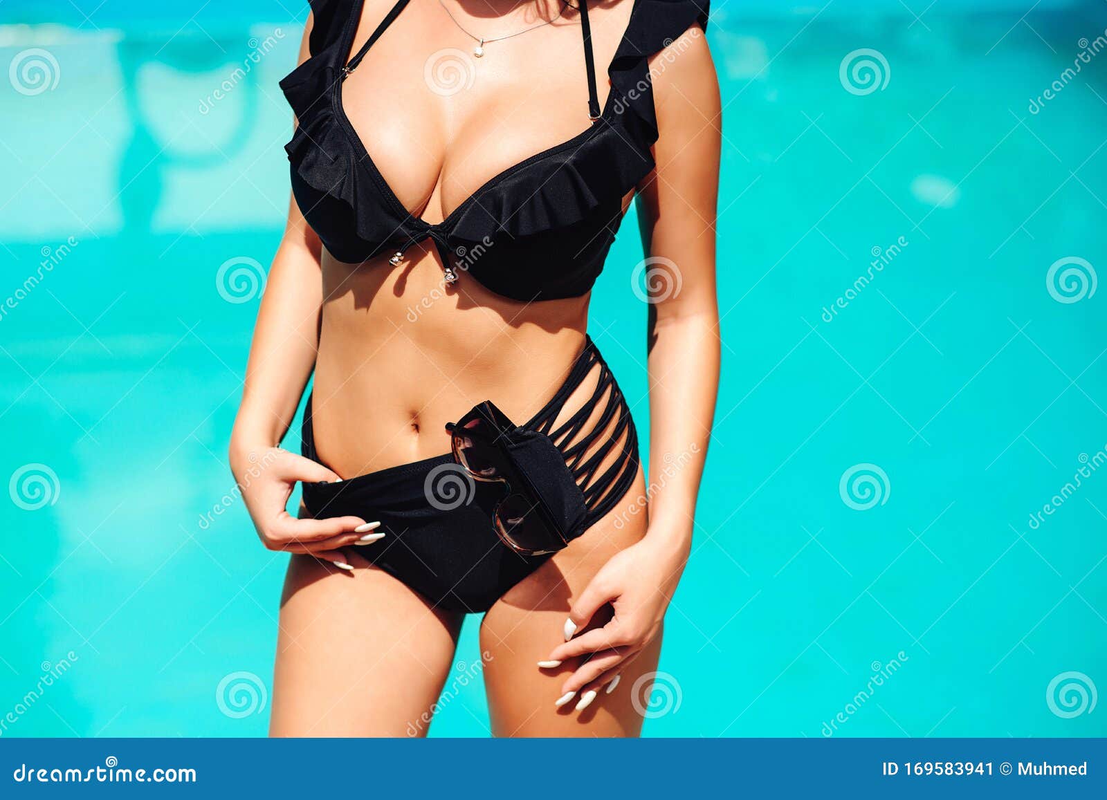 Fotografia do Stock: Sexy brunette woman with big tits in swimsuit posing  in swimming pool at hot summer. Beautiful sexy hot girl with perfect body  and big boobs posing in fashionable black