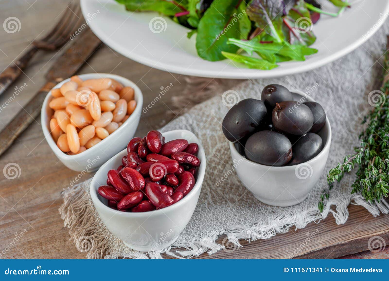 beans are white and red with large black olives in white small cups with green leaves of arugula and lollo ross prepared